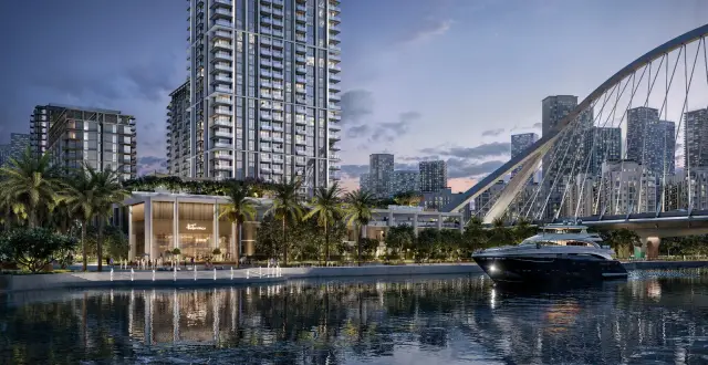 Arlo tower rising above the Dubai Creek Harbour waterfront at dusk, with the arched bridge and a yacht on the canal